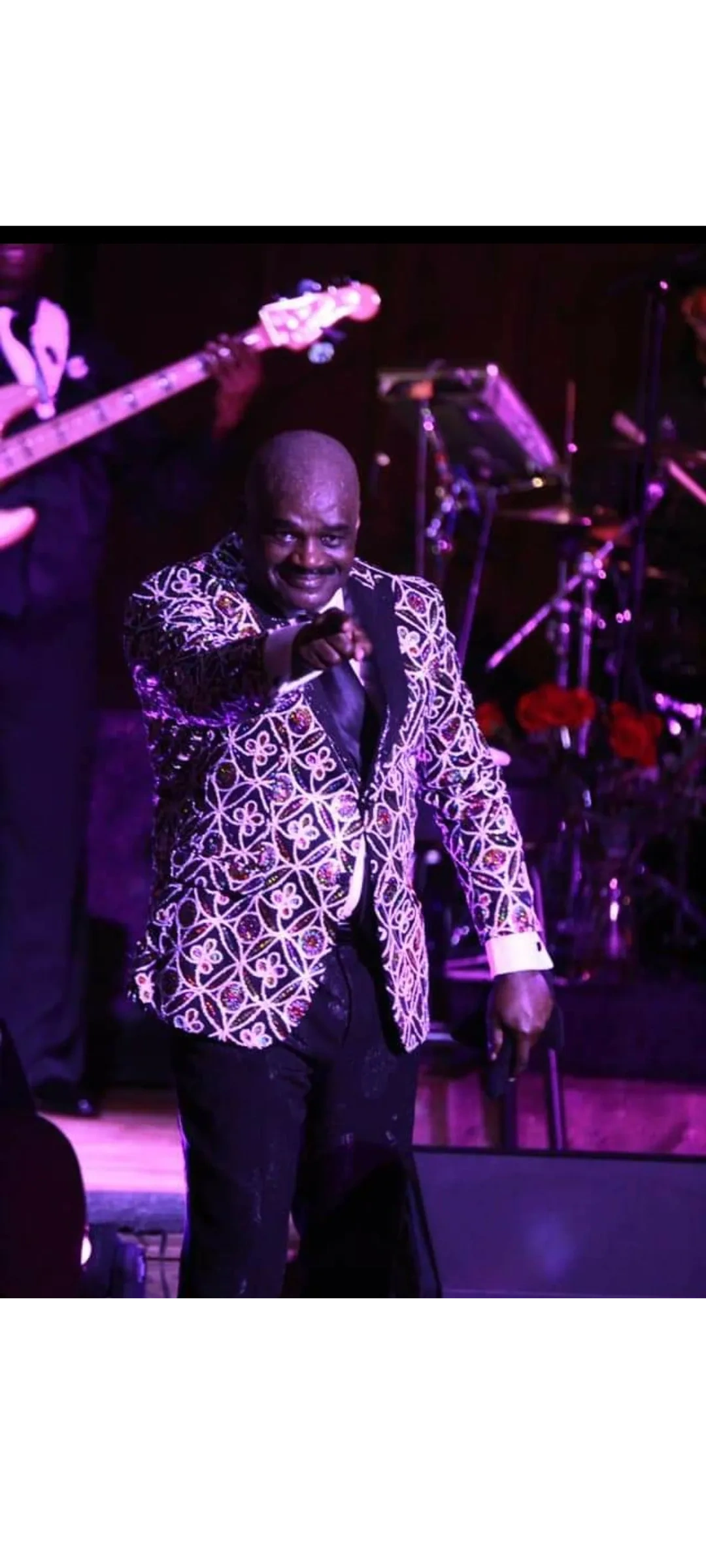 Julius Williams performing live on stage in ornate patterned blazer