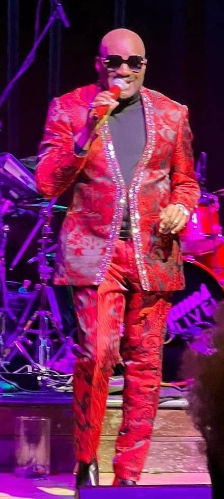 Julius Williams in red sequined suit performing on stage with purple lighting